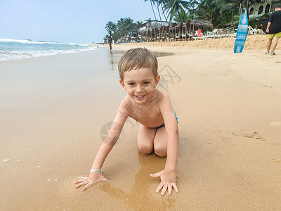小男孩坐在海边湿沙滩上微笑图片