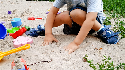 吹号子的男孩幼儿男孩玩具和在公园沙箱中挖子的肖像背景
