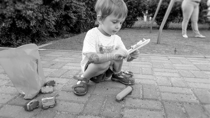 小男孩坐在公园的地上玩玩具车的黑白肖像图片