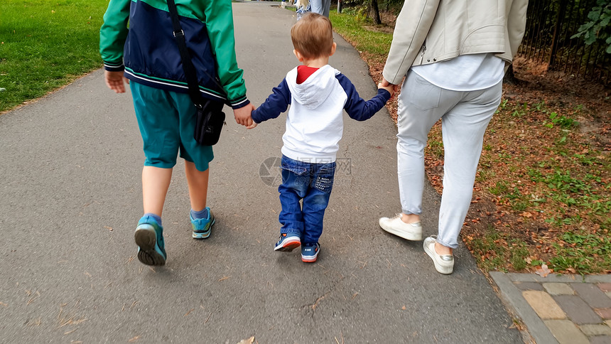 欢乐家庭与幼儿男孩握着手在公园中行走的照片图片