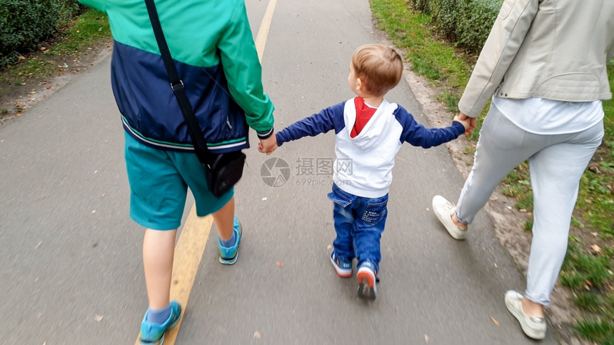 欢乐家庭与幼儿男孩握着手在公园中行走的照片图片