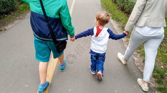 欢乐家庭与幼儿男孩握着手在公园中行走的照片图片