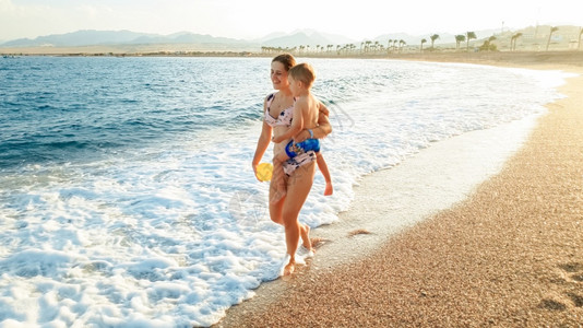 照片中年轻女拥抱小儿子并展示他在海滩面的美丽日落图片