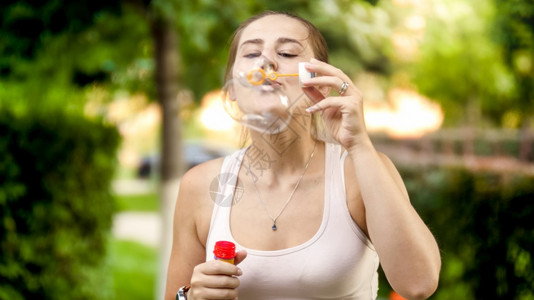 快乐的微笑女人肖像在夏日公园吹着彩色肥皂泡沫快乐的微笑年轻女人肖像在夏日公园吹着彩色肥皂泡沫背景图片