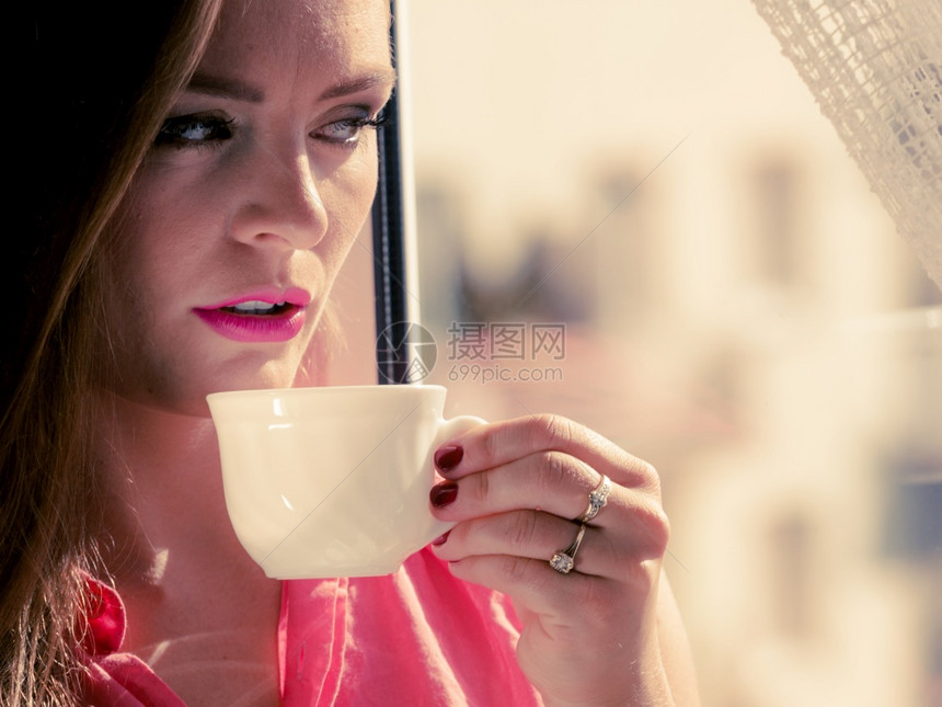 坐在窗台上的年轻女子透过窗看享受空闲时间在喝咖啡或杯茶时放松图片
