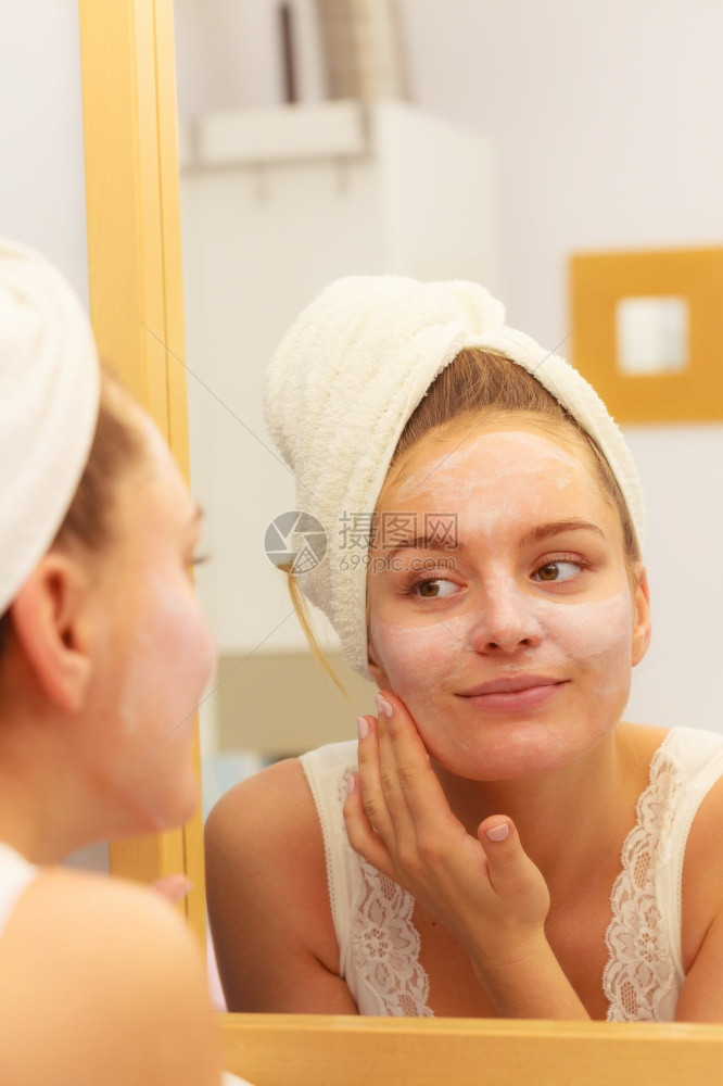 妇女用面罩湿润的皮肤霜在脸部看卫生间镜子时使用女孩要照顾她的皮肤层润湿剂皮肤科疗养妇女要在浴室里用面罩霜图片