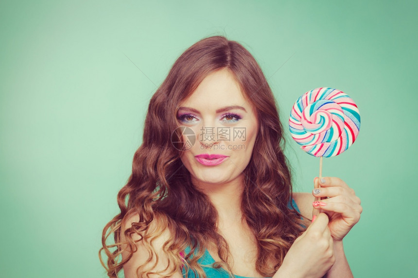 迷人的有魅力女孩拿着多彩的棒糖甜美食物和享受概念工作室拍摄的绿色蓝背景刻画的图像图片