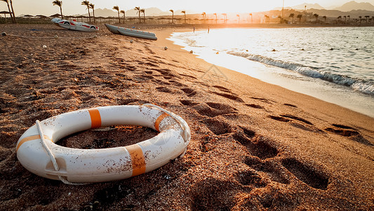 浮选紧贴近距离的照片拯救生命的戒指躺在海刺砂上美丽的日落在海洋上紧贴的拯救生命戒指图像躺在海刺沙上背景