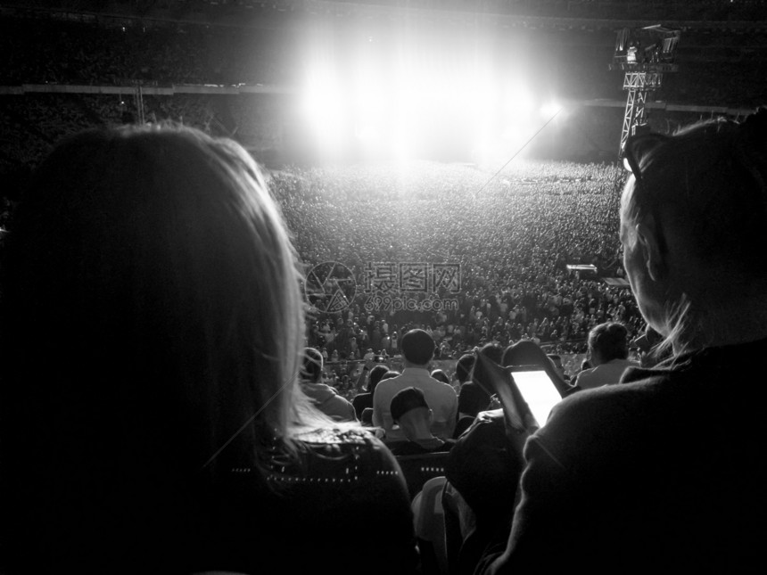 观众聚集在体育场的球迷中他们坐在体育场的支架上在晚听摇滚音乐会光和激束对准灯和激束照亮了表演场景大批球迷坐在体育场支架上在晚听摇图片