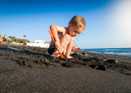 小男孩坐在海滩上玩沙子图片