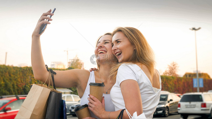 有两个笑着的姑娘用纸袋在智能手机上。图片