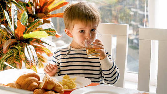 可爱的幼儿男孩吃早餐和喝苹果汁的肖像图片
