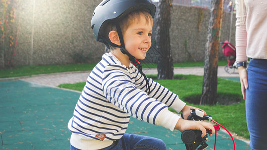 穿着黑色保护头盔的快乐微笑小男孩骑着自行车图片