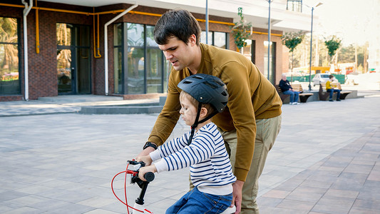 年轻父亲在教骑自行车时支持其小儿子图片