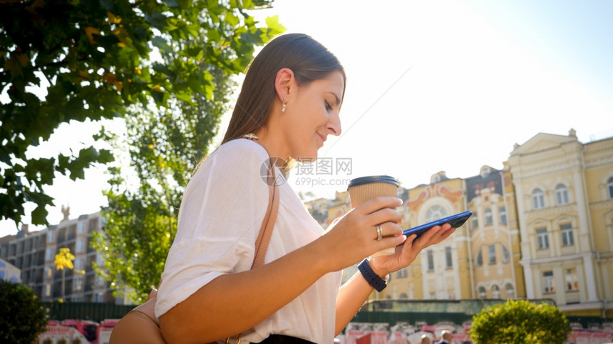 美丽的女学生用咖啡和智能手机在公园行走的肖像图片