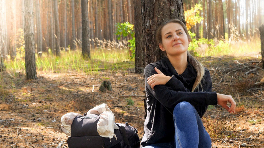 欢笑的年轻女士坐在地上靠林中的松树上图片