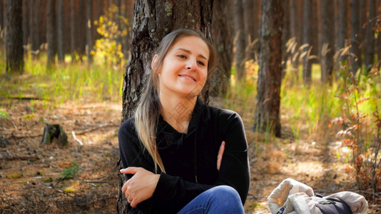 长途跋涉在森林里靠着松树的美丽微笑女人肖像图片