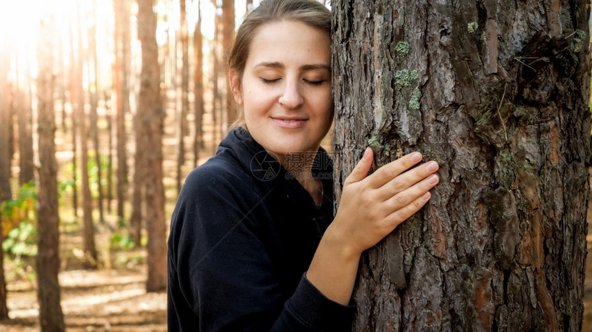 美丽的年轻女在森林中倾斜和触摸大树的肖像生态环境保护和与自然谐相处的概念美丽年轻女在森林中倾斜和触动大树的肖像生态环境保护和与自图片