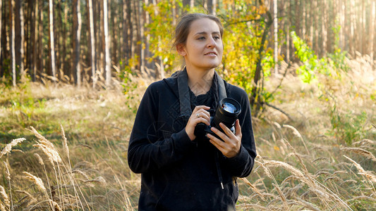 年轻女记者带着相机在森林中行走并寻找摄影情景的肖像图片