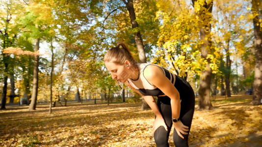 疲倦和惫的年轻女子在秋季公园慢跑时呼吸和休息图片