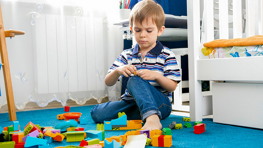 与玩具块在地毯上相邻的小集中男孩肖像与玩具块在地毯上相交的小集中男孩肖像背景图片