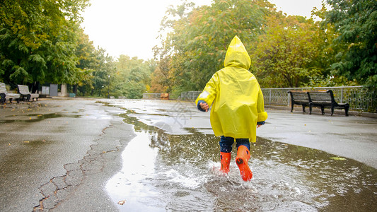孩子雨穿着橡皮靴的小男孩在公园雨后大水坑里跑来去背景