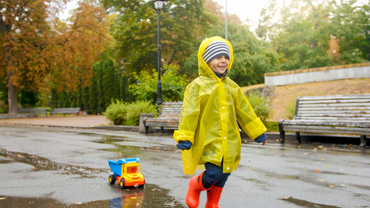 雨靴黄色带着玩具卡车在公园冲过水坑背景