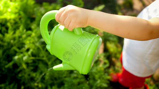拿着水壶的男孩小男孩在花园里拿着免费塑料水壶背景