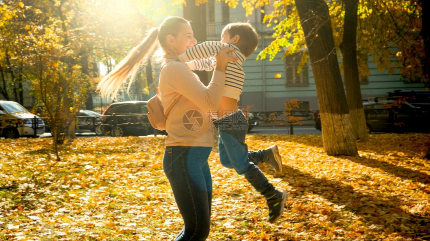 美丽的快乐母亲在秋天公园拥抱和旋转着她笑的小儿子美丽的快乐母亲在秋天公园拥抱和旋转着她笑的小儿子图片