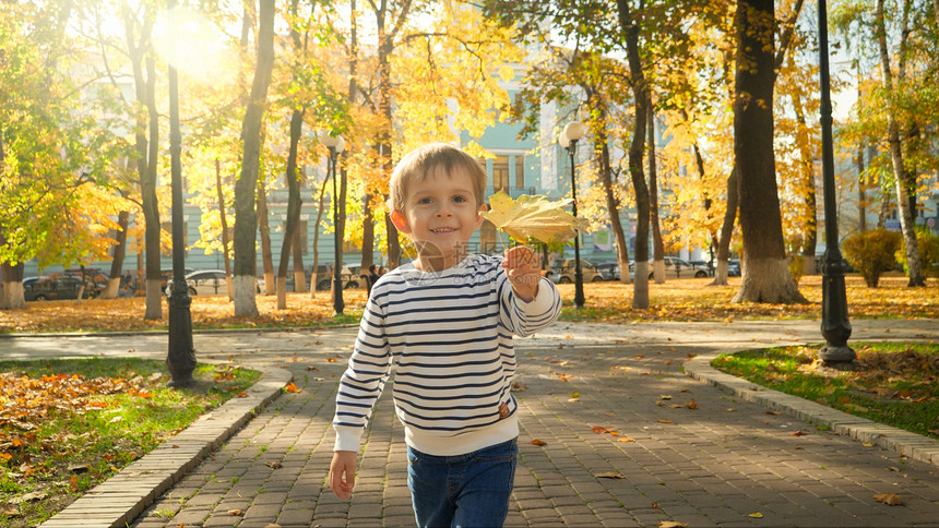 可爱男孩的肖像他拿着黄色秋天的长发朝公园摄像机跑去图片