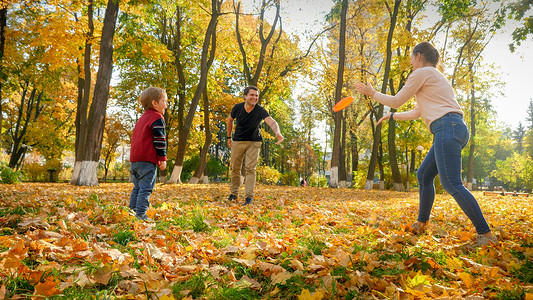 快乐的年轻父母在秋天公园的飞盘上与儿子玩耍图片