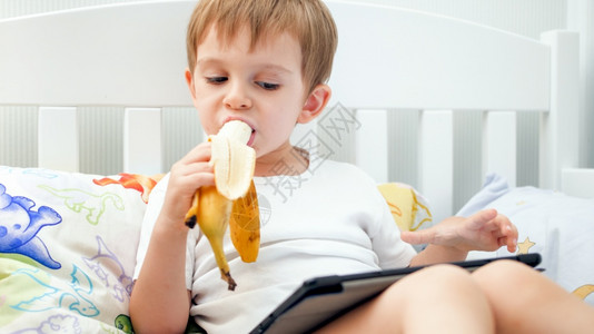 男孩在床上吃香蕉玩平板电脑图片