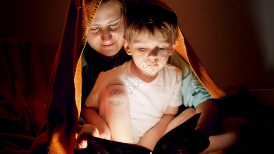 母亲与她儿子躺在毯下看故事书图片