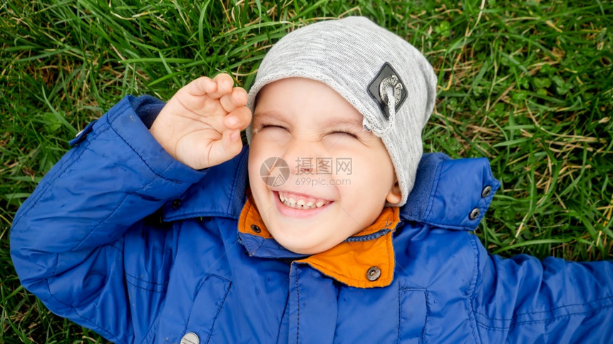 坐在田野绿草上的笑可爱男孩近照图片