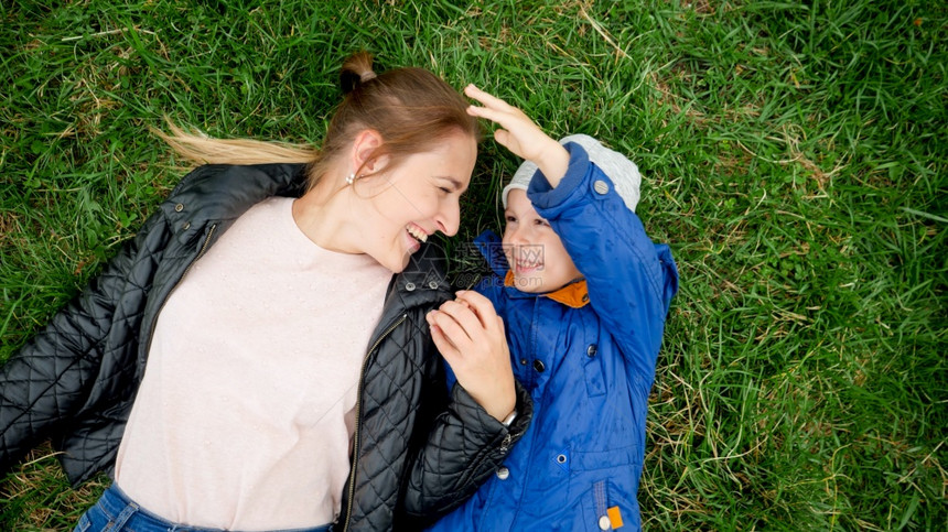 快乐的小男孩肖像年轻母亲躺在草地上玩得开心图片