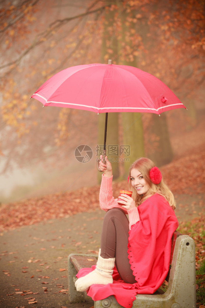 女孩坐在公园里女士拿着伞子从杯上喝咖啡坐在长椅上女孩坐在公园里拿着伞子坐在公园里图片