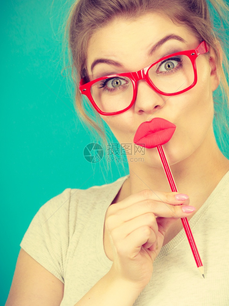 可爱的美女随意风格的书呆子眼镜戴着红色假嘴唇拿着红棒子玩戴绿色蓝照片拍下来玩狂欢节的饰品概念图片
