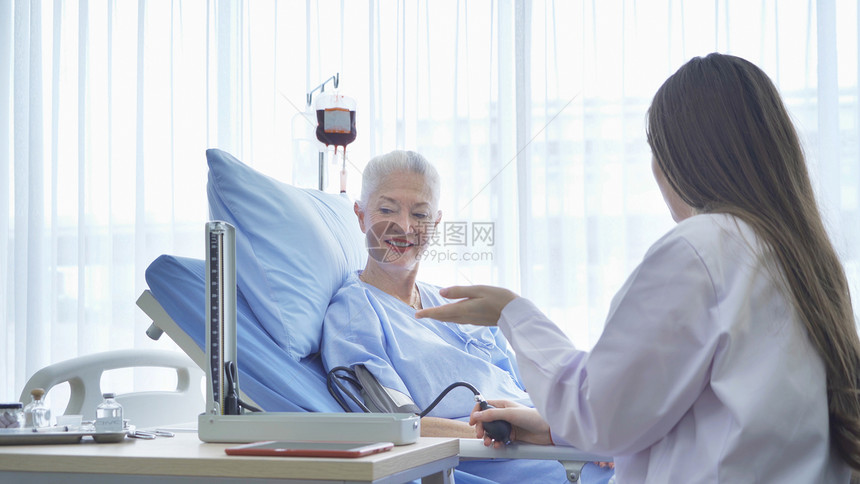 快乐的女医生检查病的老年女病人的血压测试她们躺在医院病房的床上在医疗和治概念中躺着图片