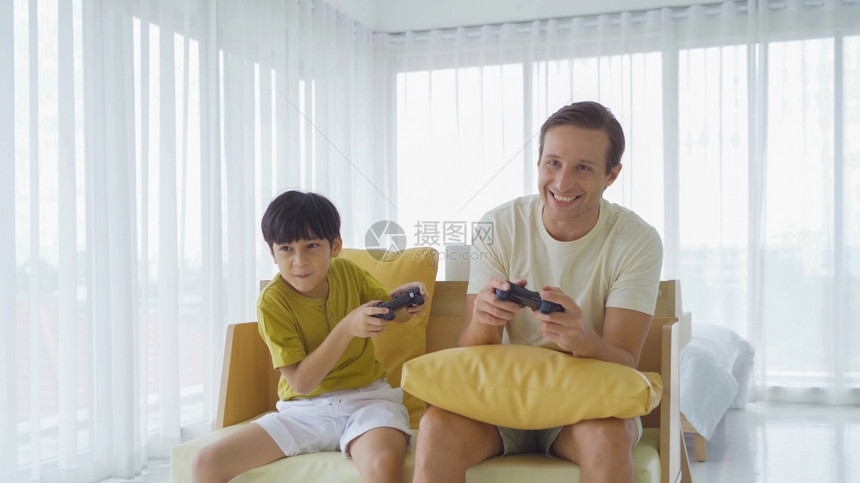 父亲和儿子身着VR或虚拟现实眼镜头戴盔坐在沙发上当着电视在家庭面前玩子游戏学习技术和创新概念图片