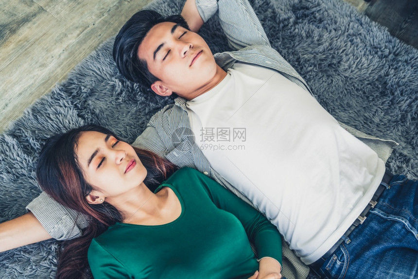 幸福的亚洲情侣躺在客厅的地毯上休息图片