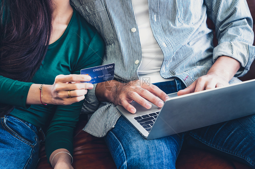 年轻夫妇在家中的互联网站上使用信卡在线购物信用卡号码是假冒的信用卡上没有个人信息网上商业购物概念图片