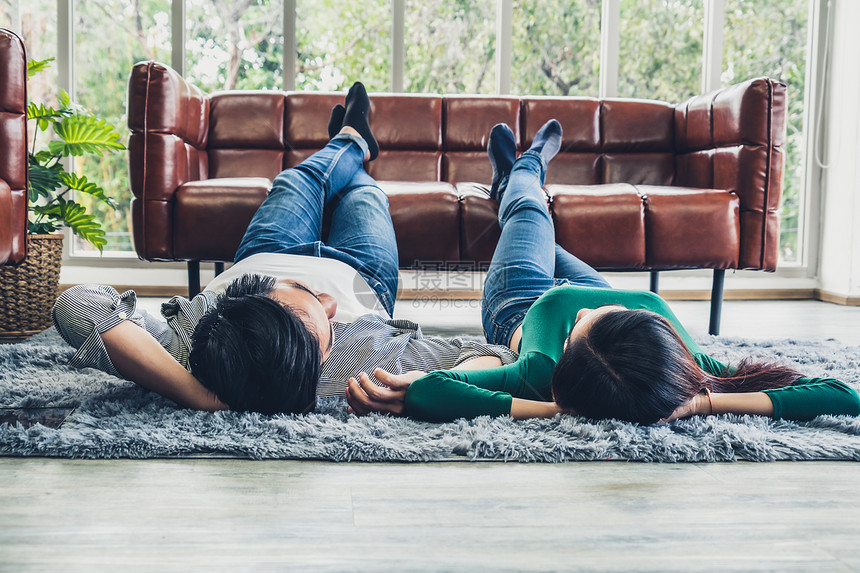 幸福的亚洲情侣躺在客厅地毯上休息图片