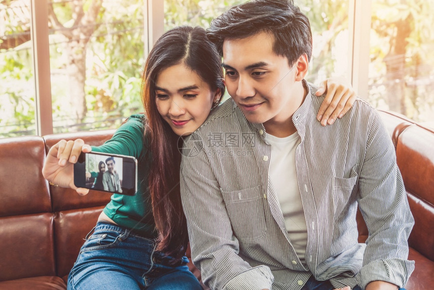 快乐的亚洲情侣在客厅用手机自拍图片