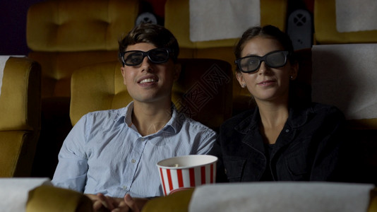 电影中的男人和女观看一部三维眼镜的电影有兴趣观看屏幕奋和吃爆米花图片