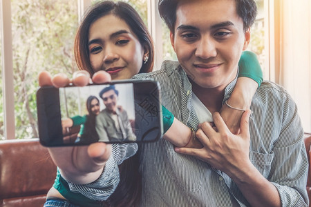 快乐的亚洲情侣在客厅用手机自拍背景图片