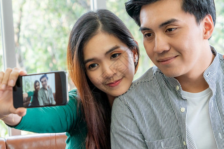 快乐的亚洲情侣喜欢在家里客厅用手机拍自照片图片