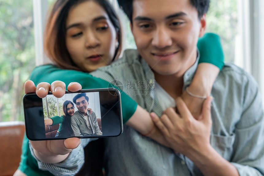 快乐的亚洲情侣喜欢在家里客厅用手机拍自照片图片