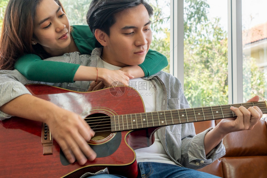 亚洲小情侣一起在家中的客厅玩吉他和唱歌音乐生活方式概念图片