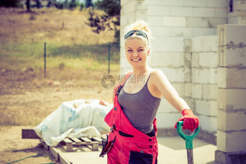 女工在业建筑地使用铲子站立在工业建筑地辛勤进行房屋翻新工作图片