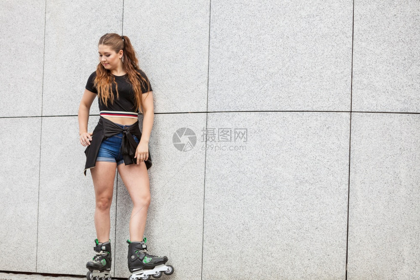 身穿溜冰鞋的年轻妇女站在城市的水泥墙上图片